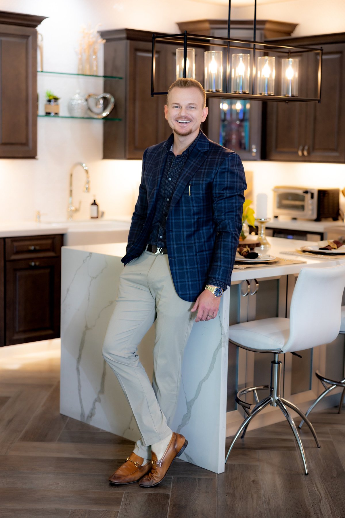 Smiling man in navy plaid blazer and light pants standing in modern kitchen