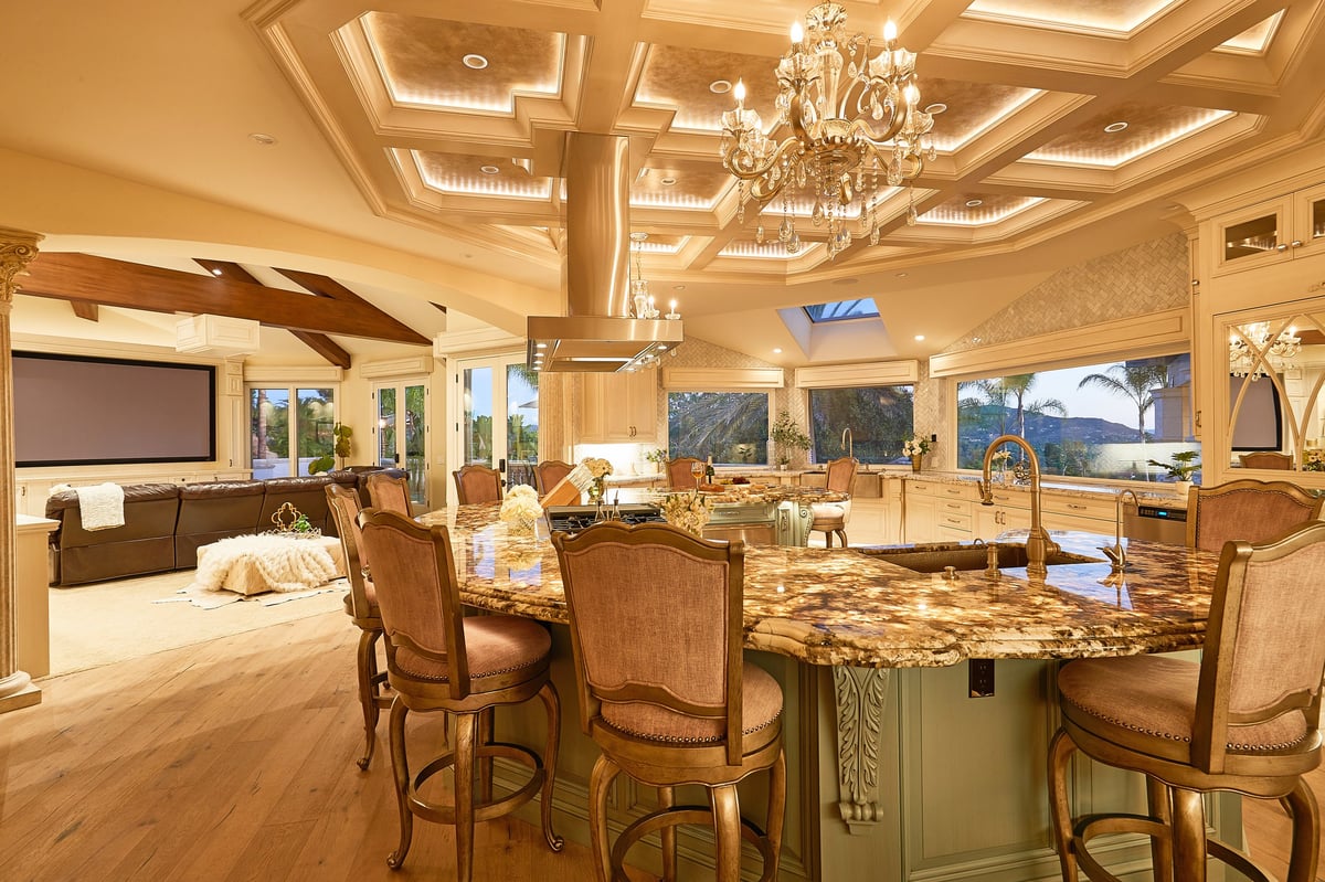 Luxurious open-concept kitchen and living room with coffered ceilings, granite island, wood furnishings, and panoramic windows overlooking mountains