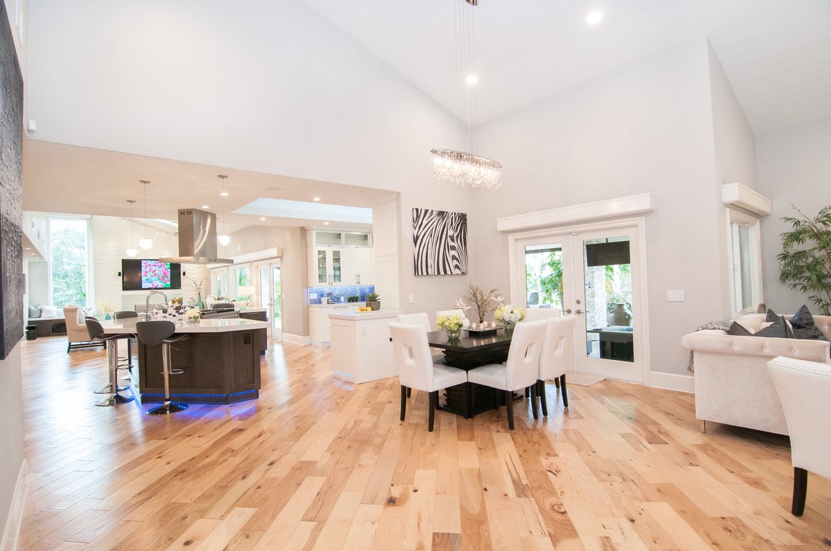 Modern open-concept home interior with hardwood flooring, kitchen island, dining area, and living room with white walls and natural lighting