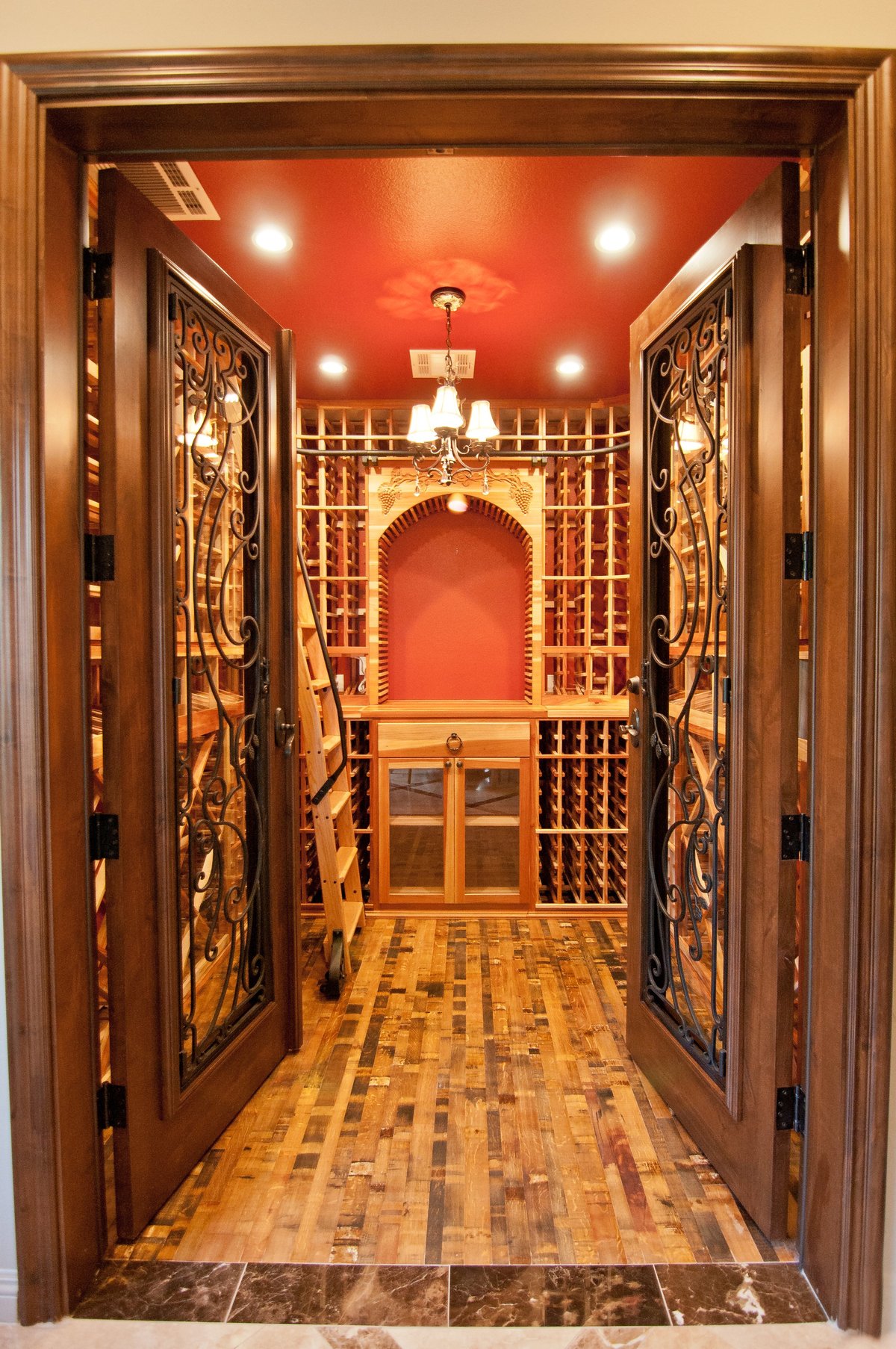 Luxurious wine cellar with red walls, ornate wooden doors, wine racks, and recessed lighting