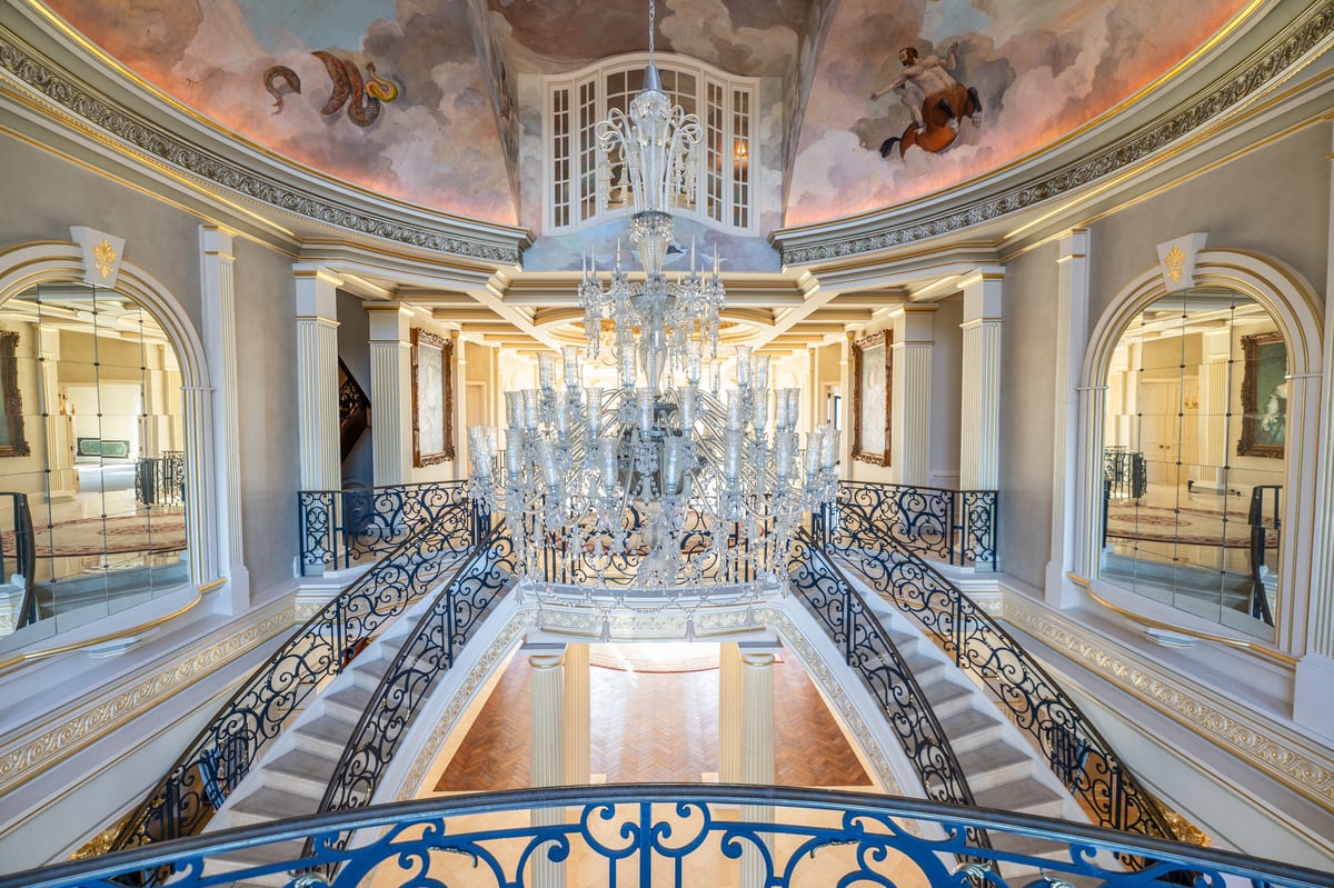Grand staircase with ornate railings and a crystal chandelier in a luxurious neoclassical interior