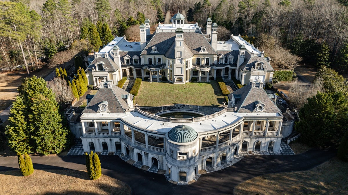 Aerial view of a grand neoclassical mansion surrounded by manicured grounds and tall evergreen trees